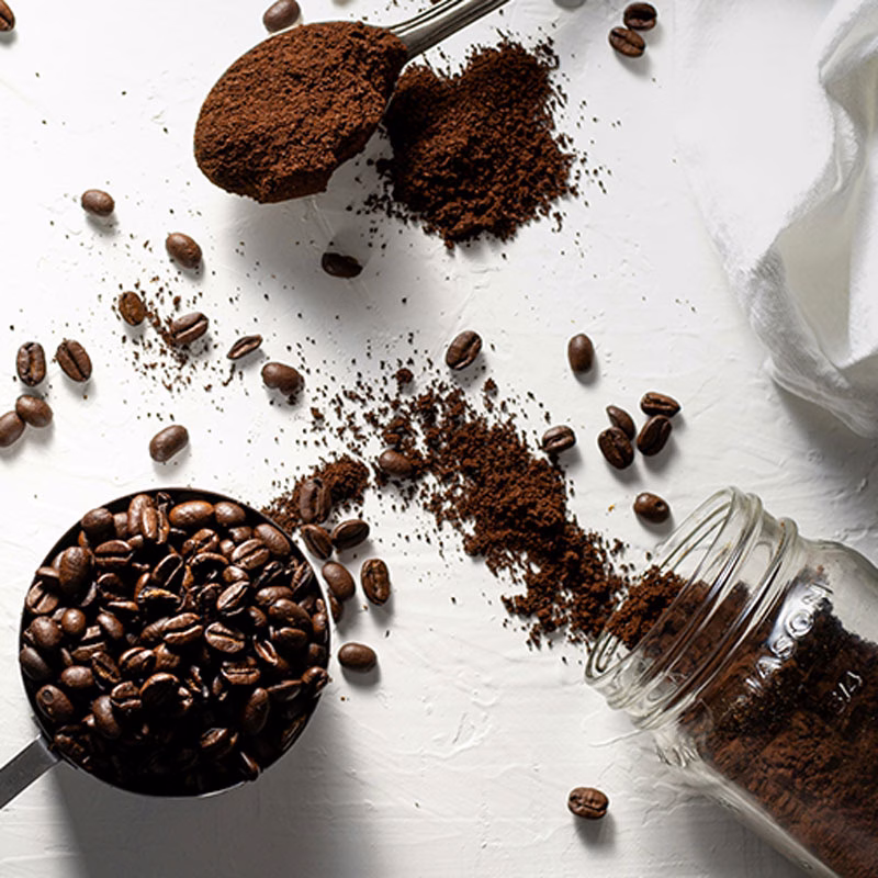 gemahlener Kaffee und Kaffeebohnen sind in Bechern und auf einem Löffel verteilt